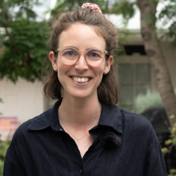 Outdoor headshot of a smiling woman with brown hair, wearing a black top.
